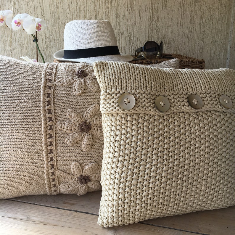May include: Two knitted throw pillows, one with a crocheted floral design and the other with a simple knit texture and decorative buttons.