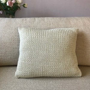 May include: A light green knitted throw pillow with a textured surface. The pillow is sitting on a beige couch.