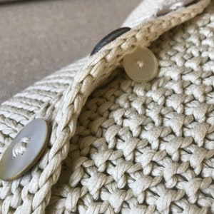 May include: Close-up of a beige knitted fabric with two white buttons. The fabric is woven in a tight, textured pattern.