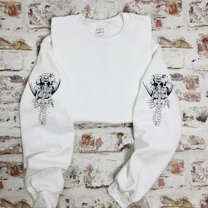May include: White sweatshirt with a black skeleton mermaid graphic on each sleeve.