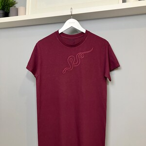 May include: A maroon t-shirt with a red embroidered snake design on the front.