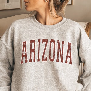 May include: A gray sweatshirt with the word "ARIZONA" printed in maroon on the front.
