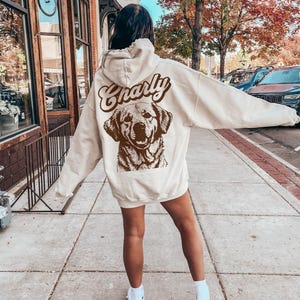 May include: A cream-colored hoodie with a brown graphic of a dog and the word "Charly" in a retro font.