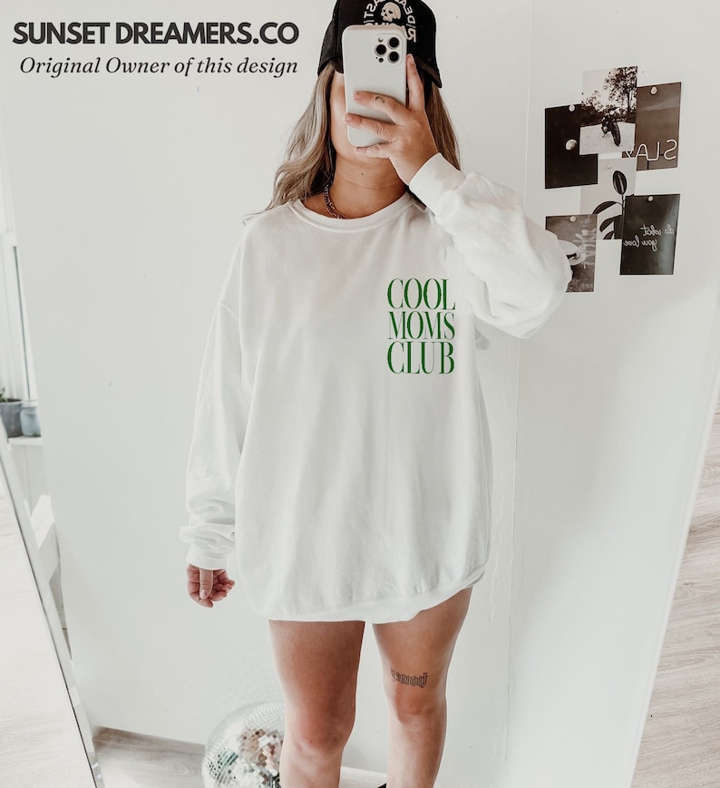 May include: White long-sleeved sweatshirt with the text "COOL MOMS CLUB" in green letters.