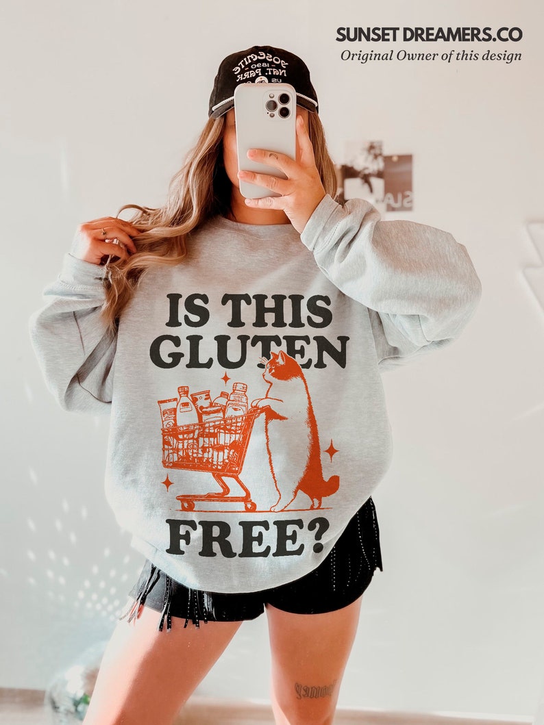 May include: A gray sweatshirt with a graphic of a cat pushing a shopping cart full of food items. The text "IS THIS GLUTEN FREE?" is printed on the sweatshirt.