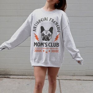 May include: Gray sweatshirt with a black and white graphic of a French bulldog. The graphic says "Antisocial Frenchie Mom's Club" with a lightning bolt on each side of the text. The text "Exclusive Frenchie Mom Society" is below the graphic.