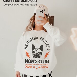 May include: White sweatshirt with a black and white graphic of a French bulldog with the text "Antisocial Frenchie Mom's Club Exclusive Frenchie Mom Society" in orange and black.