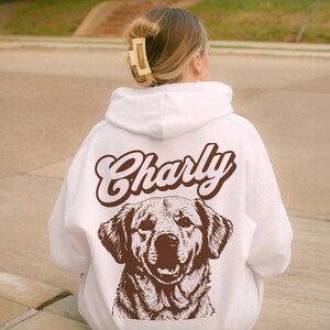 May include: White hoodie with a brown illustration of a dog and the name "Charly" in brown text.