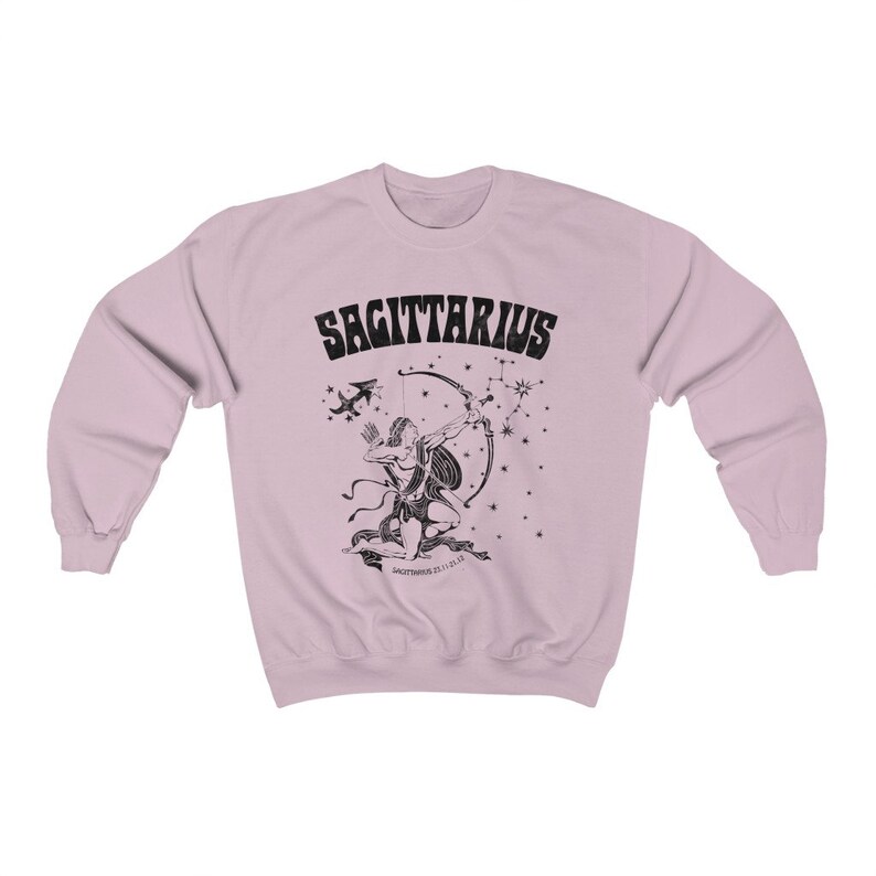 May include: Pale pink sweatshirt with a black Sagittarius design. The graphic shows an archer with a bow and arrow, constellations, and the word "SAGITTARIUS". The design is a vintage style.