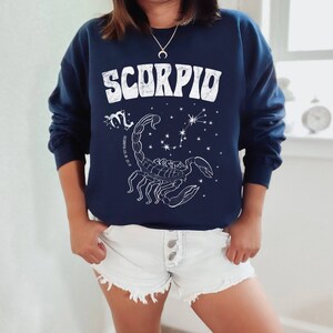 May include: Navy blue sweatshirt with a white graphic of a scorpion and the word "SCORPIO" in a retro font. The graphic also includes the constellation Scorpio and the dates "October 23 to November 21."