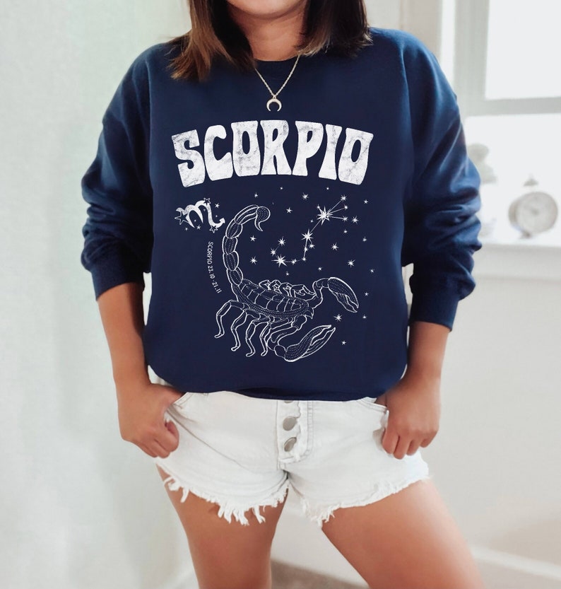 May include: Navy blue sweatshirt with a white graphic of a scorpion and the word "SCORPIO" in a retro font. The graphic also includes the constellation Scorpio and the dates "October 23 to November 21."