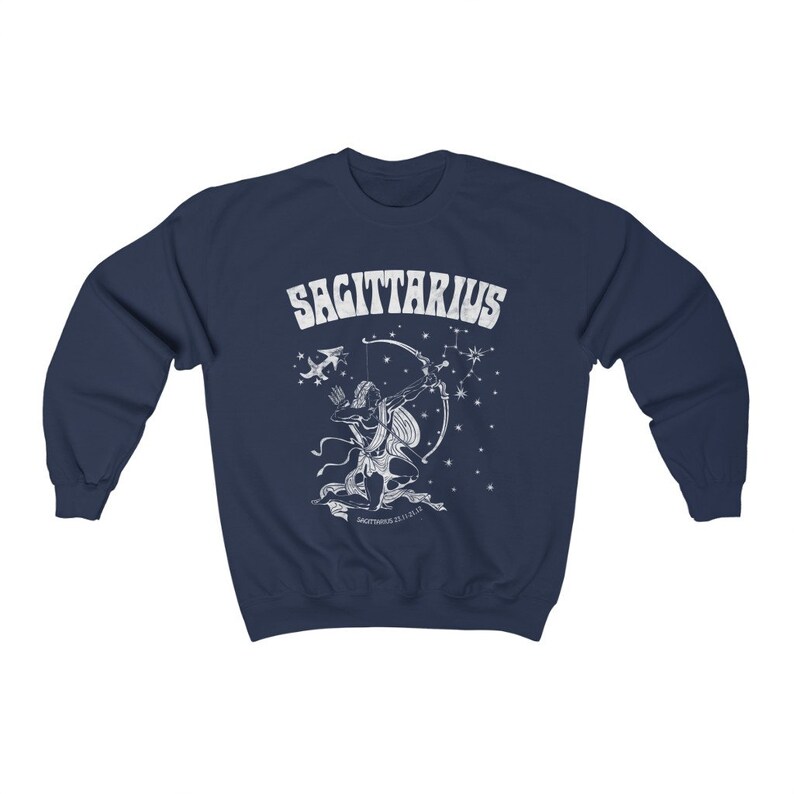 May include: Navy blue sweatshirt with a white Sagittarius zodiac design. The graphic depicts an archer with a bow and arrow, the word "SAGITTARIUS", and star constellations. A comfortable garment for those interested in astrology.