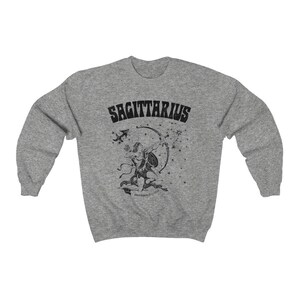 May include: A grey sweatshirt with a black Sagittarius design. The graphic features the word "SAGITTARIUS" above an archer with a bow and arrow, and a constellation of stars. The design is printed on a comfortable, casual sweatshirt.