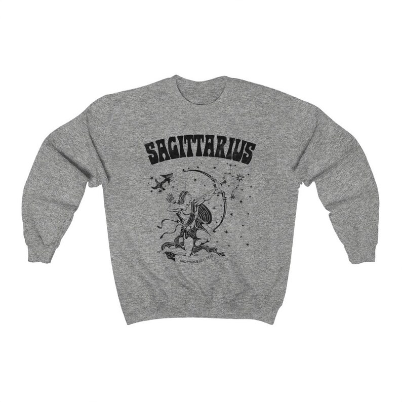 May include: A grey sweatshirt with a black Sagittarius design. The graphic features the word "SAGITTARIUS" above an archer with a bow and arrow, and a constellation of stars. The design is printed on a comfortable, casual sweatshirt.