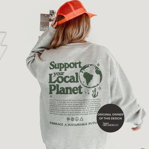 May include: Gray sweatshirt with a green graphic print of the Earth and the text "Support Your Local Planet". The text below the graphic reads "Planet Earth is one of the most unique planets in our solar system, it has the will to overcome adverse events and sustain some of the most unique life forms ever known. Although the earth seems nearly invincible, we all need to do our part to maintain this beautiful rock. As many people know, Good things don't last forever. Do your part, Ride a bike or walk instead of short driving, pick up litter, dispose less waste, take only what you need and enjoy what we have. Embrace a Sustainable Future". The bottom of the graphic reads "Original Owner of this Design Sweet Dreamers Co."
