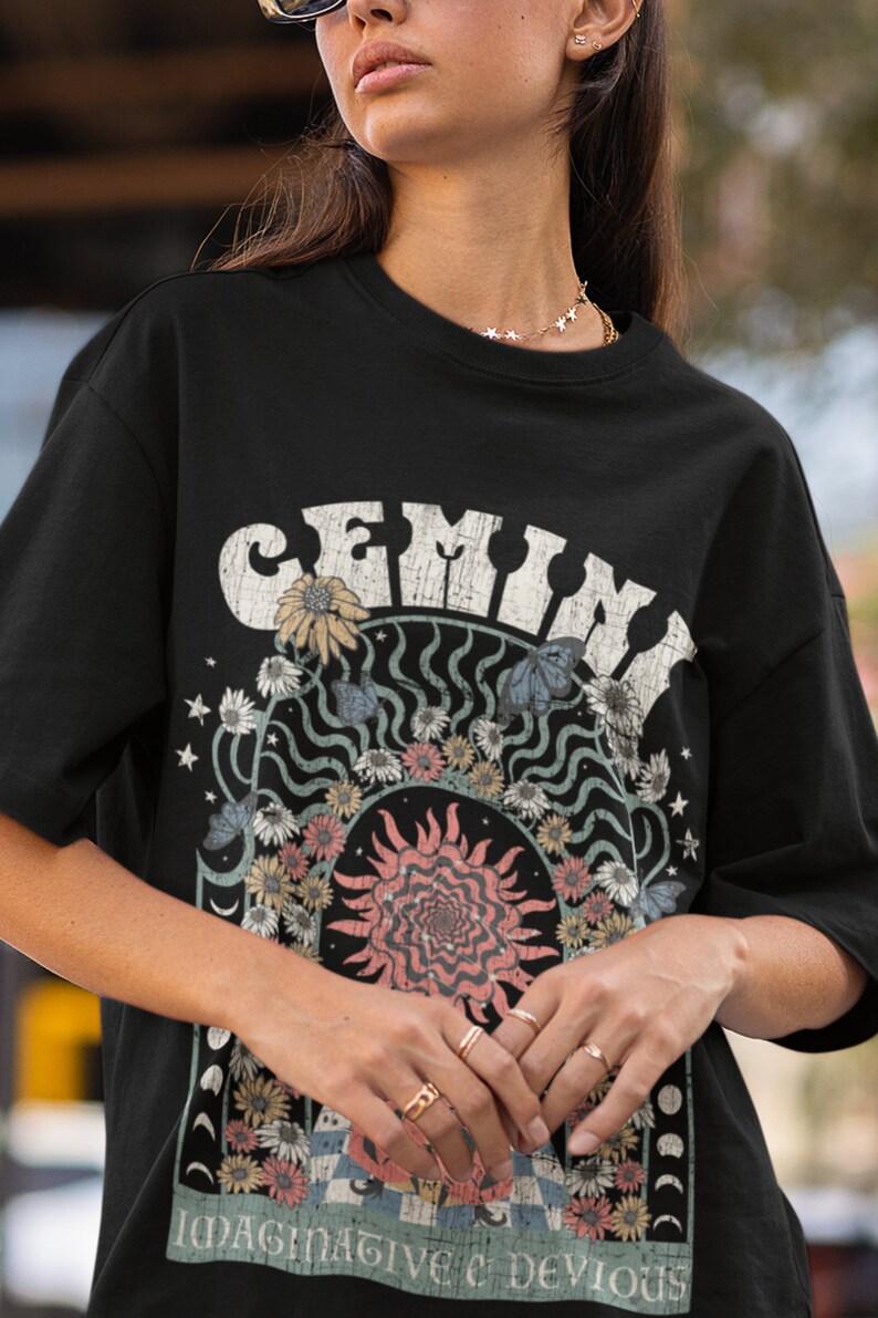 May include: Black t-shirt with a vintage graphic. The design features the word "GEMINI" in distressed white lettering, a sun, flowers, butterflies, and the text "IMAGINATIVE & DEVIOUS".