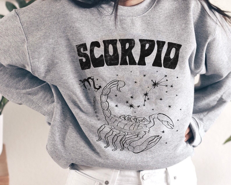 May include: Gray sweatshirt with a black graphic of the zodiac sign Scorpio. The graphic includes the constellation and the text "Scorpio 23.10 - 21.11".