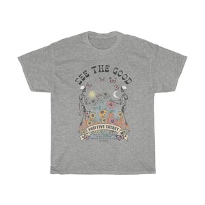 May include: A heather gray t-shirt with a graphic design. The design features two skeletons, flowers, butterflies, and the words "SEE THE GOOD" and "POSITIVE ENERGY". The shirt has a crew neck and short sleeves.