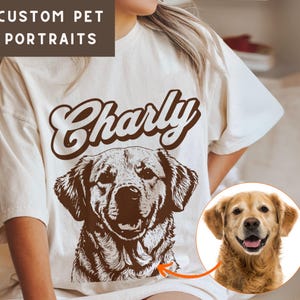 May include: A white t-shirt with a brown illustration of a dog and the name "Charly" printed in brown. The dog is a golden retriever with a happy expression.