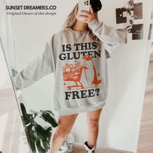May include: A gray sweatshirt with the text "Is this gluten free?" in black and orange. A cartoon cat is pushing a shopping cart full of groceries.