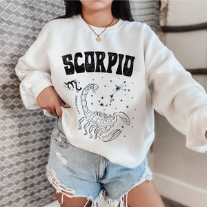 May include: White sweatshirt with a black graphic of a scorpion and the word "Scorpio" in a retro font. The graphic also includes the constellation Scorpio and the dates "October 23 - November 21".