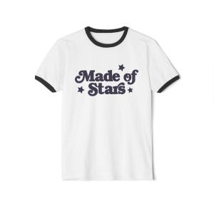 May include: White t-shirt with a black ringer neck. The shirt has a navy blue graphic that says "Made of Stars" with stars on either side of the text.