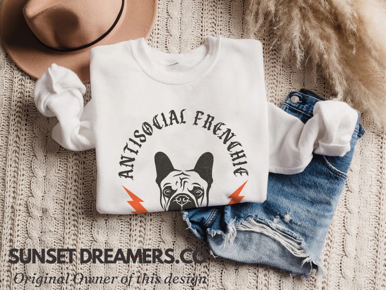 May include: White sweatshirt with a black and white illustration of a French bulldog's head with the text "Antisocial Frenchie" in a black gothic font.