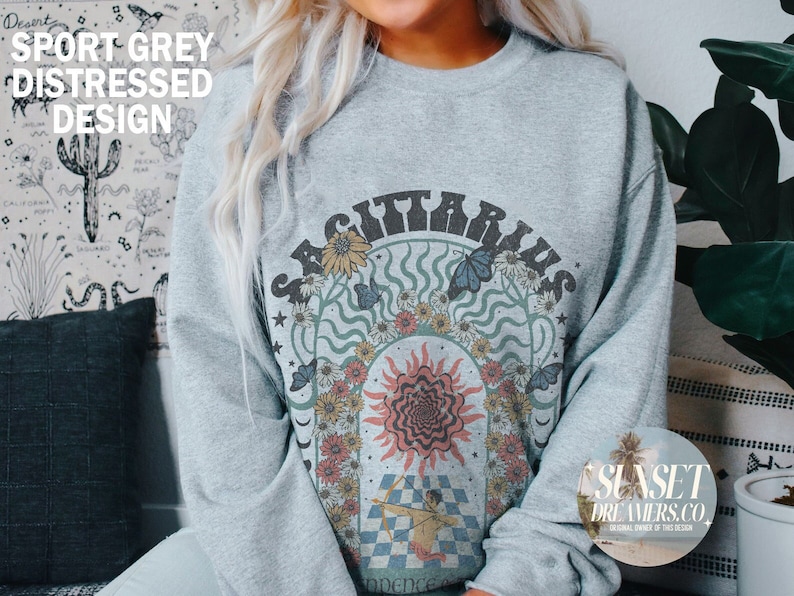 May include: Sport grey distressed design sweatshirt featuring a Sagittarius graphic. The design includes the word "SAGITTARIUS" above a sun, flowers, butterflies, and an archer. The sweatshirt has a crew neck and long sleeves.