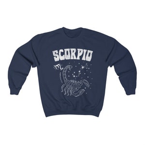 May include: Navy blue sweatshirt with a white graphic of a scorpion and the word "SCORPIO" in a retro font. The graphic also includes the astrological symbol for Scorpio and the dates October 23 - November 21.
