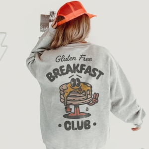 May include: A gray sweatshirt with a graphic of a cartoon pancake stack with the text "Gluten Free Breakfast Club".