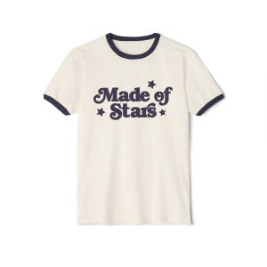 May include: A white t-shirt with a navy blue ringer and the text "Made of Stars" in a retro font with stars on either side.