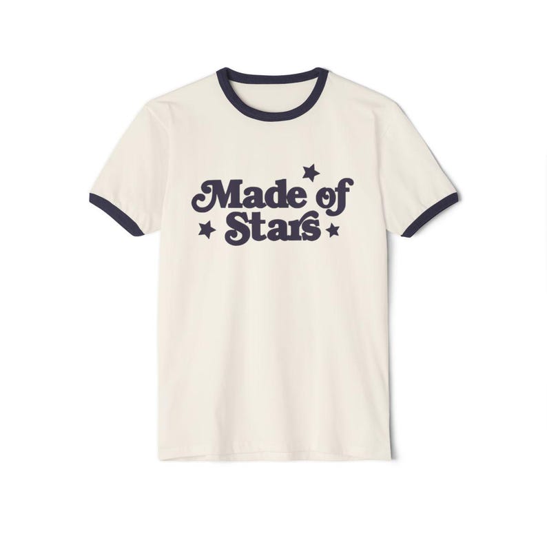 May include: A white t-shirt with a navy blue ringer and the text "Made of Stars" in a retro font with stars on either side.