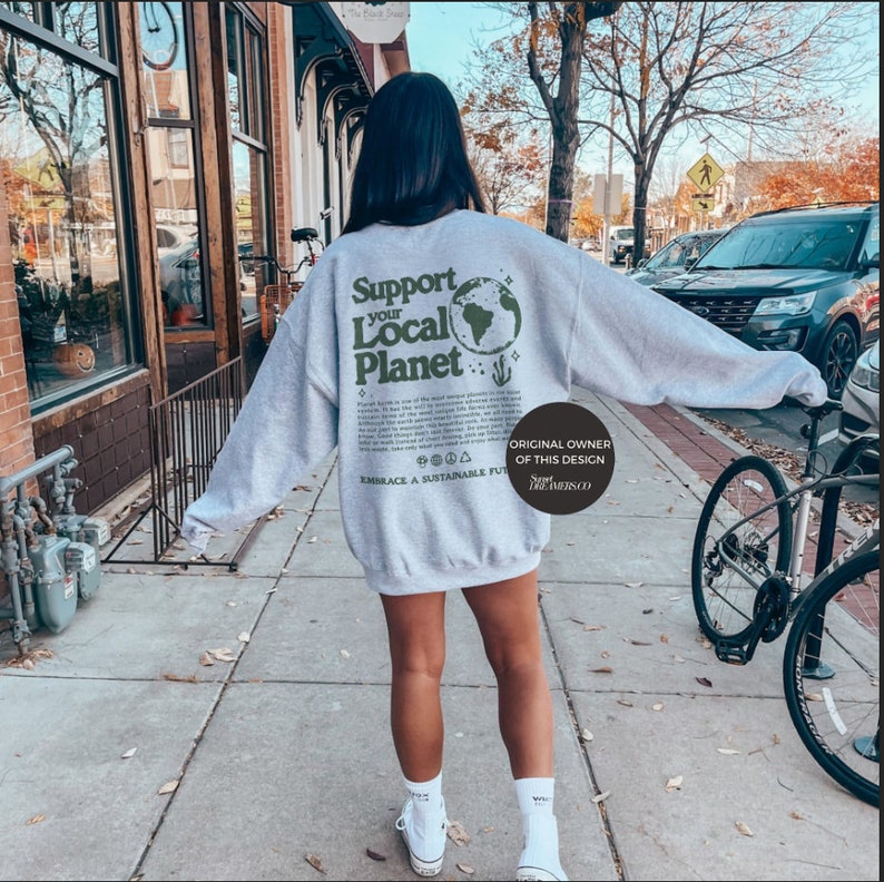 Puede incluir: Una sudadera gris con el texto "Support your Local Planet" y un gr&aacute;fico de un globo terr&aacute;queo verde. El texto "Embrace a Sustainable Future" tambi&eacute;n est&aacute; impreso en la sudadera. El propietario original del dise&ntilde;o es "Support the Locals Co."