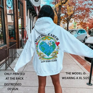 May include: White hoodie with a distressed design featuring a graphic of a heart-shaped Earth with the text "Mother Earth Lovers Club" printed on the back.