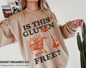 May include: A tan sweatshirt with the text "Is this gluten free?" in black and orange. A cartoon cat is pushing a shopping cart full of groceries.