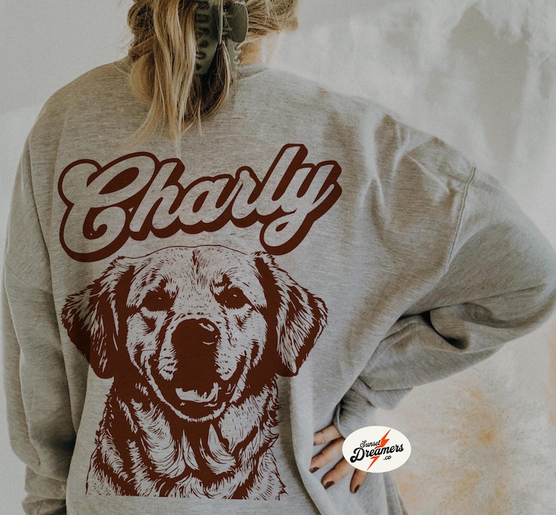 May include: A gray sweatshirt with the word "Charly" in brown script on the back. A brown illustration of a dog's head is below the text.
