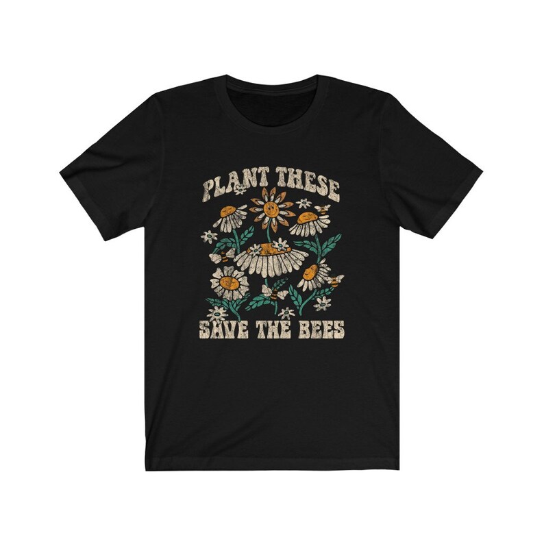 May include: Black t-shirt with a floral design featuring daisies and bees. The text "PLANT THESE SAVE THE BEES" is printed above and below the floral graphic in a vintage style.