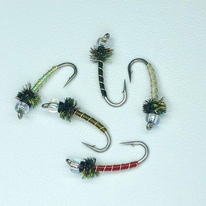 May include: Five fly fishing lures with different colored bodies and beads. The lures are tied with green, brown, red, and gold thread.