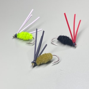 May include: Three fly fishing lures with different colored bodies and feathers. The lures are tied with black, green, and red feathers.