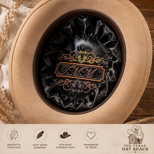 Puede incluir: Un sombrero de vaquero color canela con un forro interior de satén negro y un monograma naranja bordado que dice FMM. El forro está fruncido en los bordes e incluye bordados decorativos de volutas alrededor del texto central.