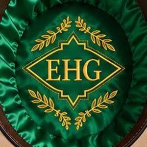 Op de afbeelding: Een beige hoed met een donkerbruine leren zweetband en een levendige jagergroene satijnen voering. De binnenkant heeft een centraal ruitvormig embleem met de goud geborduurde letters EHG, omringd door gouden lauriertakmotieven en een strik.