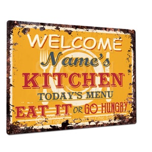 May include: A yellow and red metal sign with the text "Welcome Name's Kitchen Today's Menu Eat It or Go Hungry". The sign has a distressed, vintage look.