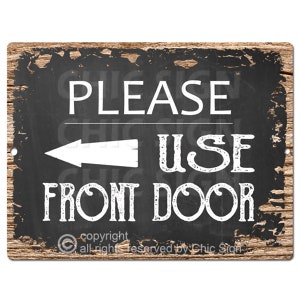 May include: Black and white metal sign with a distressed woodgrain background. The sign reads "Please Use Front Door" with a white arrow pointing to the left. The sign has a copyright notice at the bottom.