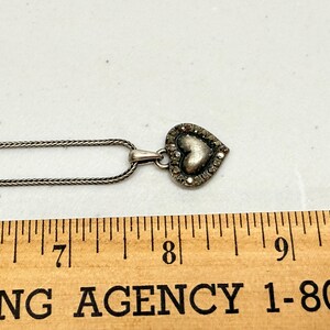 Puede incluir: Collar con colgante de coraz&oacute;n plateado. El colgante de coraz&oacute;n est&aacute; incrustado con peque&ntilde;as piedras transparentes alrededor del borde y tiene un centro texturizado. La cadena es de estilo fino y tejido. El colgante mide aproximadamente 2 cm de ancho.