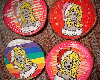 May include: Four round wooden ornaments with a painted portrait of a woman with blonde hair. Each ornament has a different background color and design, including a rainbow, red, and pink. The woman is wearing a Santa hat on two of the ornaments.
