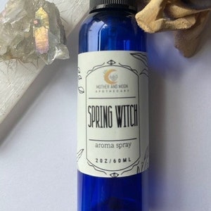 May include: A blue glass bottle with a black spray top and a white label that reads "Spring Witch Aroma Spray 2 oz/60 ml" and "Mother and Moon Apothecary".