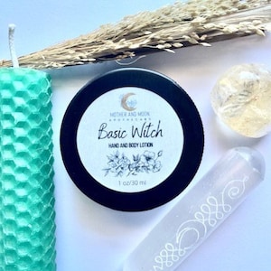 May include: A green honeycomb candle, a white crystal wand with a design, a clear crystal, and a white jar with a black lid and the text "Basic Witch Hand and Body Lotion 1 oz/30 ml" on a white background.