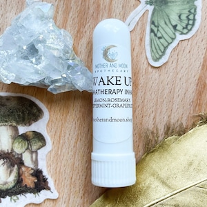May include: White aromatherapy inhaler stick with the text "MOTHER AND MOON APOTHECARY WAKE UP MATHERAPY INHA LEMON-ROSEMARY. PPERMINT-GRAPEFRUT motherandmoon.shop" printed on the label.