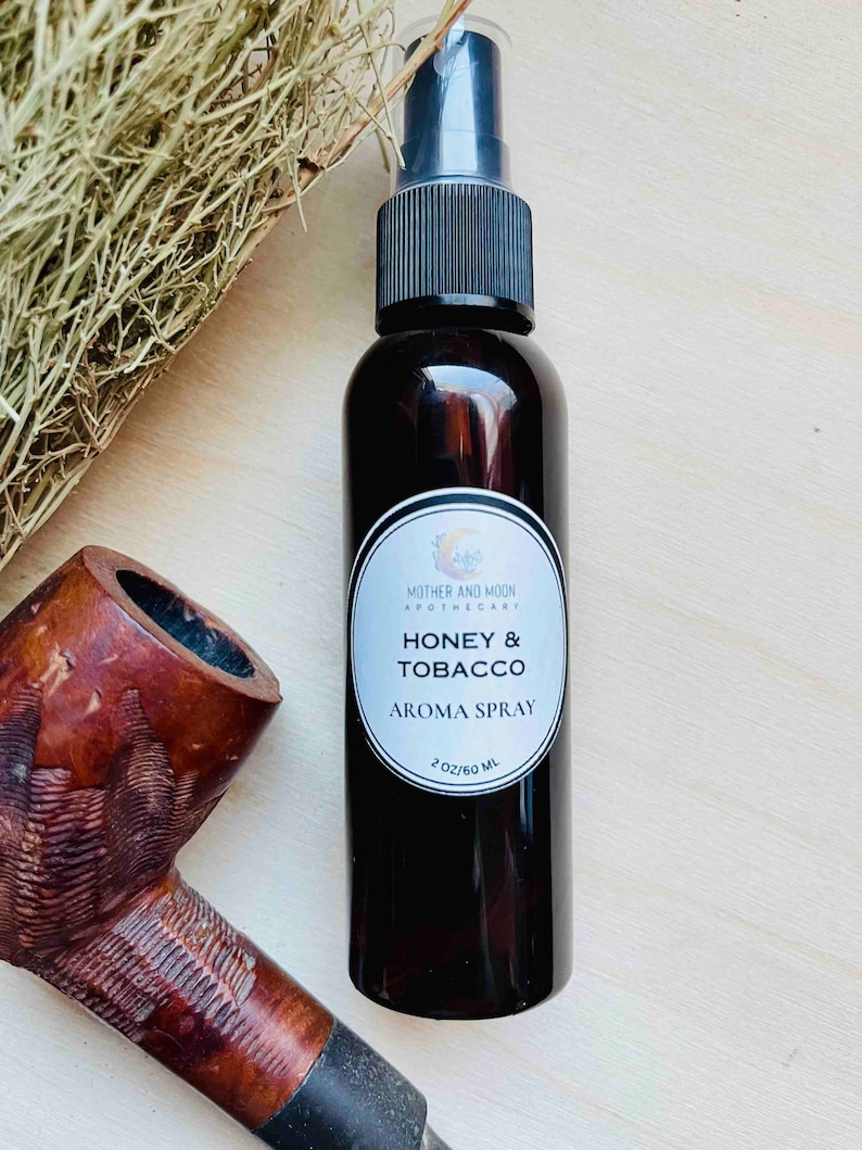 May include: A brown glass bottle with a black spray top and a white label that reads "Mother and Moon Apothecary Honey & Tobacco Aroma Spray 2 oz/60 ml".