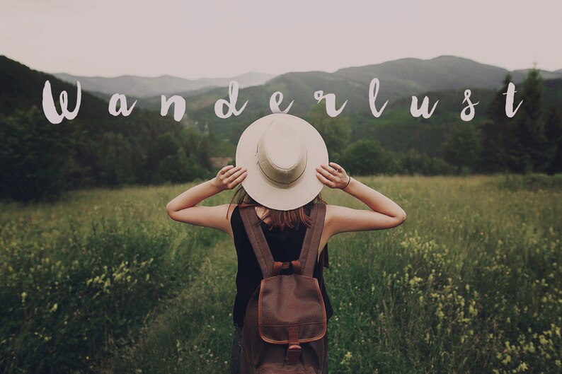 May include: A person wearing a white hat and a brown backpack stands in a field with green grass and mountains in the background. The word "wanderlust" is written in white letters across the top of the image.